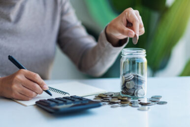 Closeup image of a woman putting coins in a glass jar , calculat