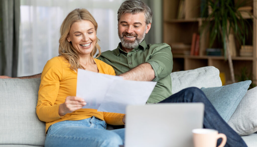 Family Insurance Concept. Happy Middle Aged Couple Reading Documents At Home