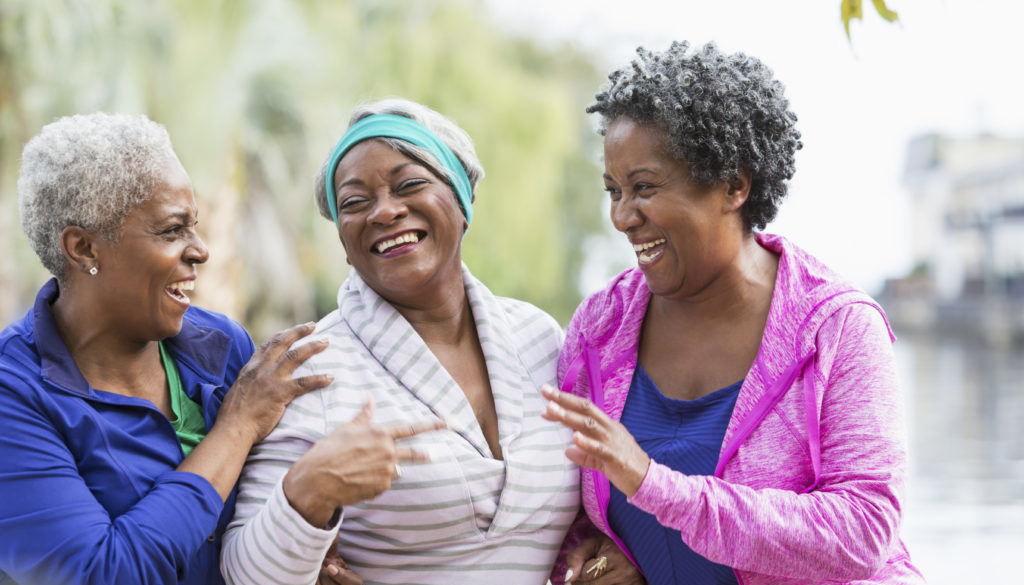 Three senior black women laughing together outdoors